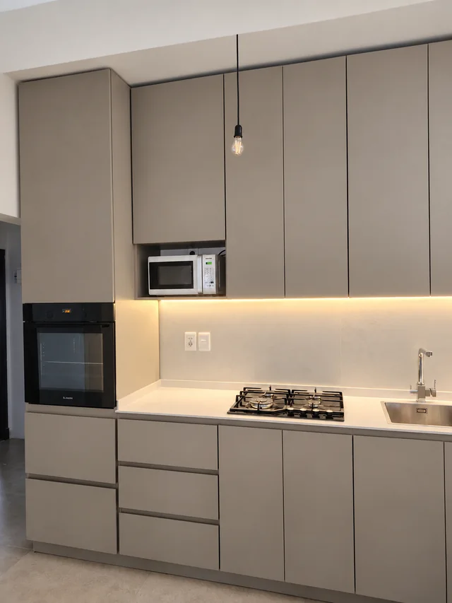 Cocina gris con muebles hasta el techo, horno empotrado, iluminación bajo los aéreos y mesada blanca.