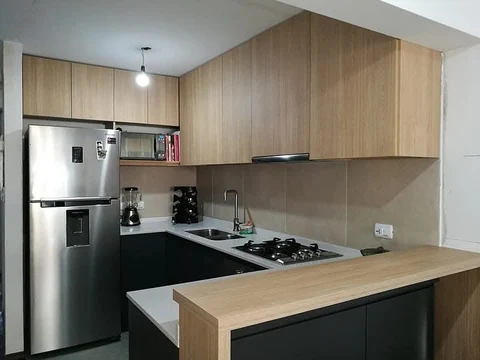 Cocina en L con aéreos de aspecto madera, muebles inferiores negros y barra de madera.